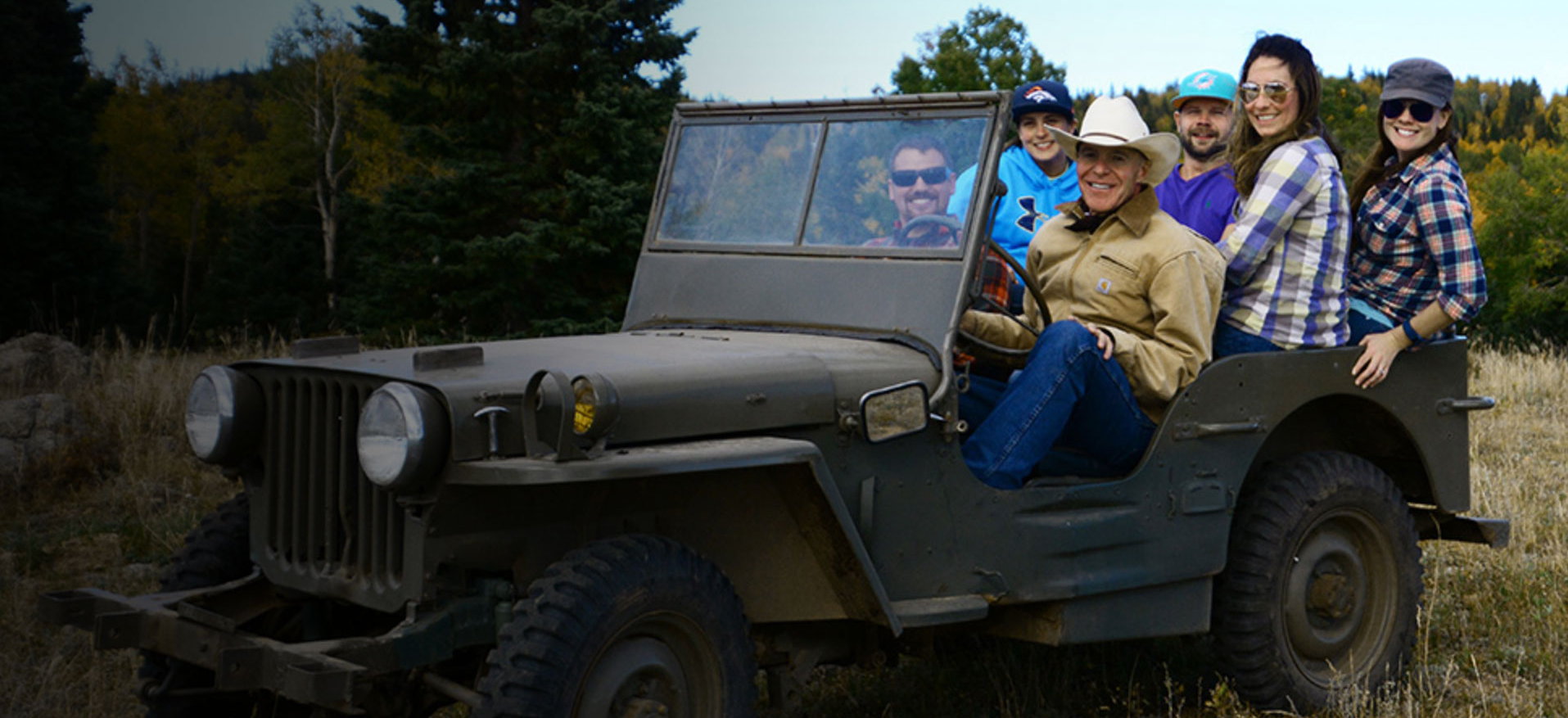 Guests riding in an open vintage Jeep on a ranch two-track at Elk Glade