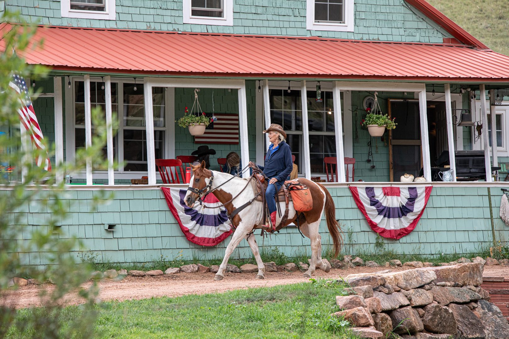 A young rider on a paint horse passing the flag-draped lodge porch