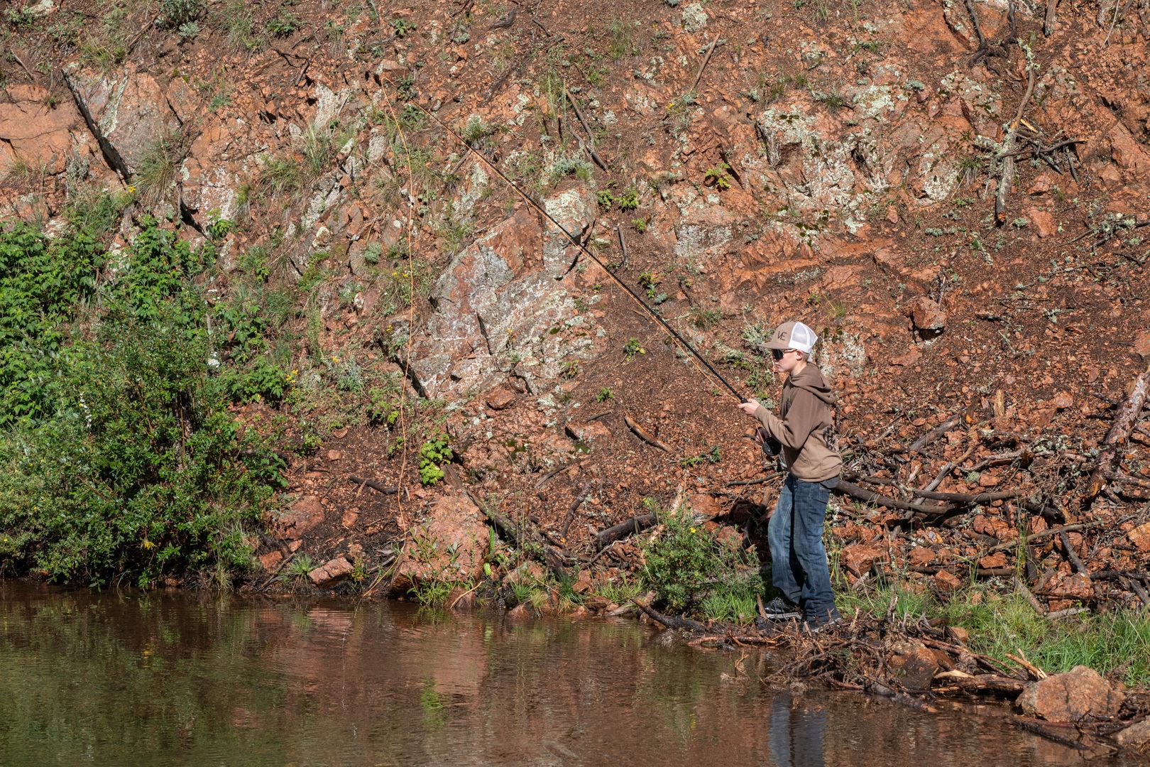 A young angler casting from the bank below a red rock face at Elk Glade
