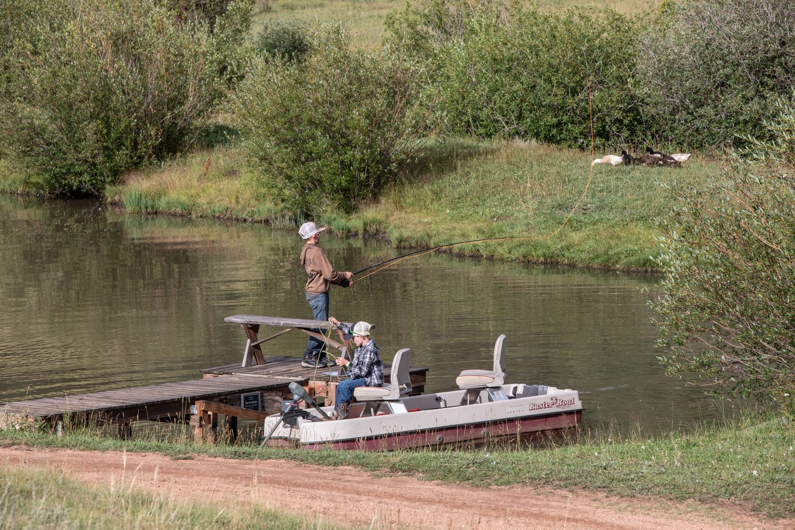 Guests fishing from the dock and a paddle boat on the lodge pond