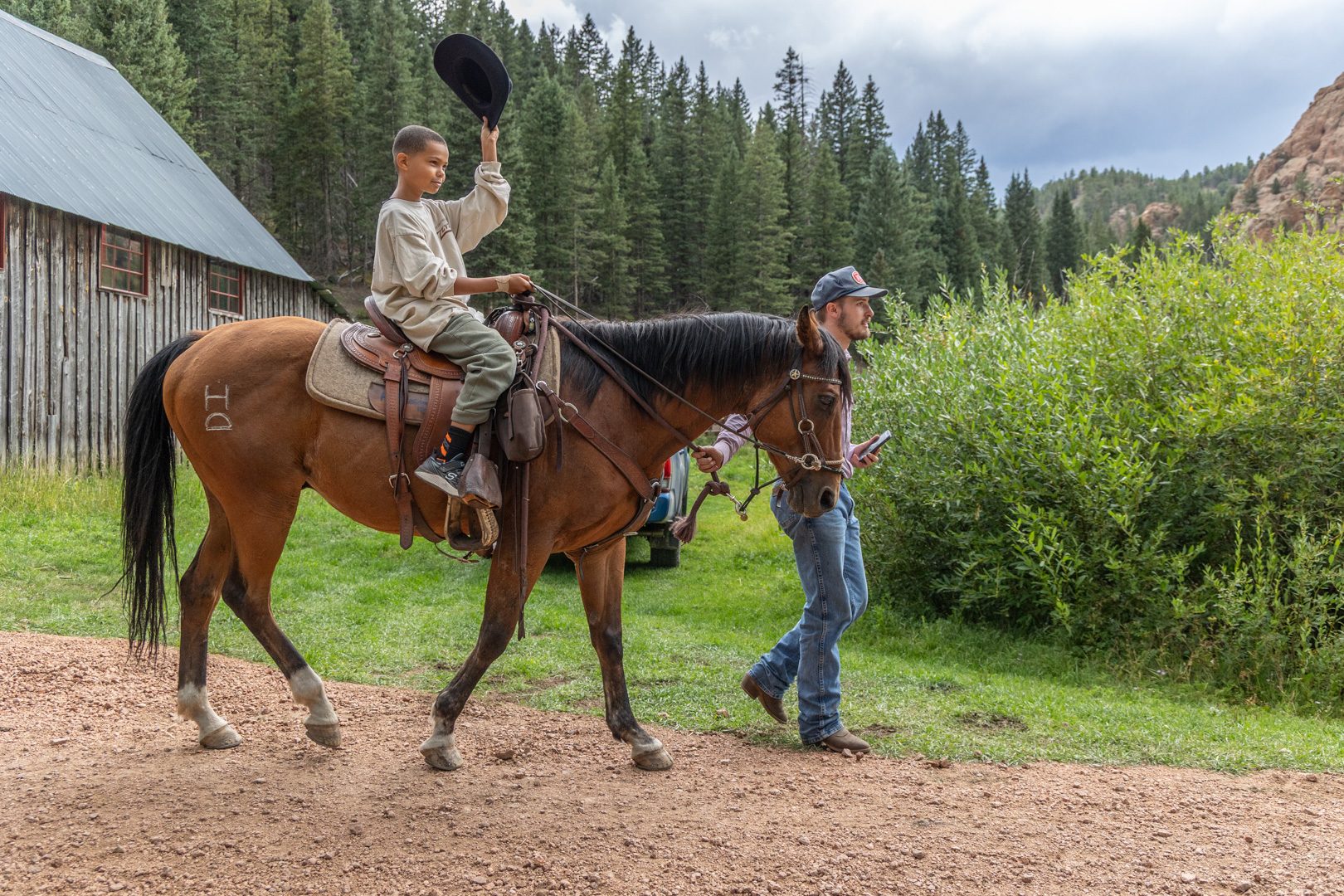 A young rider on a bay horse, led back toward the barn by a wrangler
