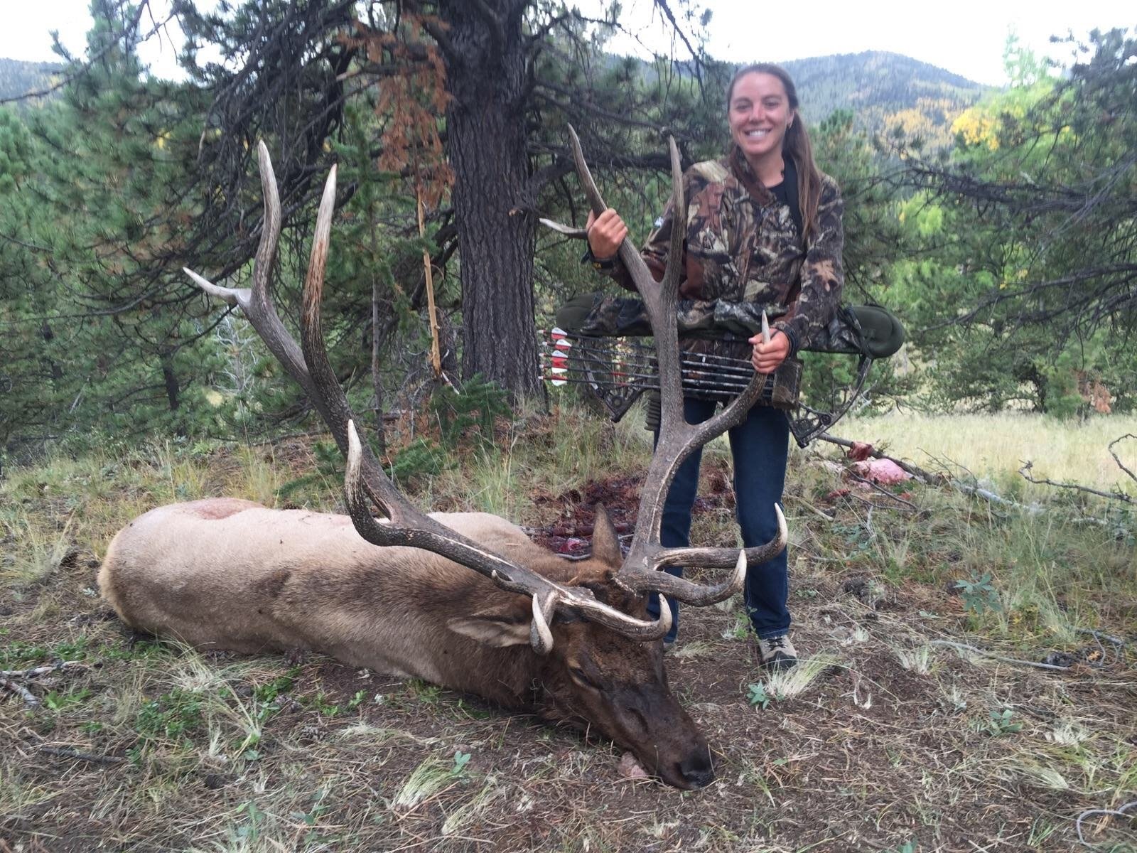 A bowhunter with her bull elk in the timber at Elk Glade